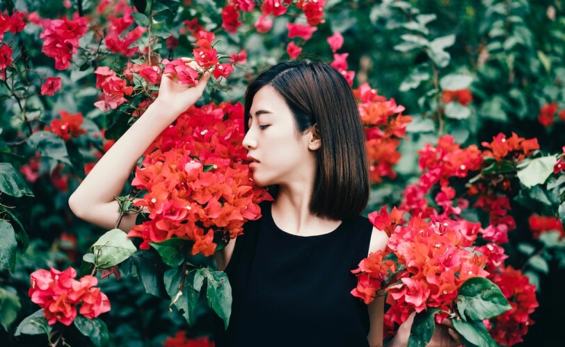 Woman standing against a bush of red flowers